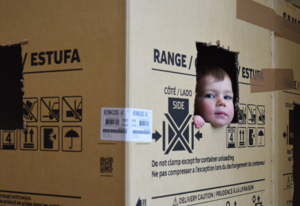 A child peeping out of carved hole in a cardboard box