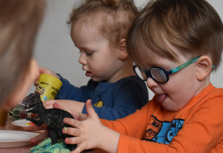 child with glasses playing with toy dinosaur and play-doh with tongue sticking out
