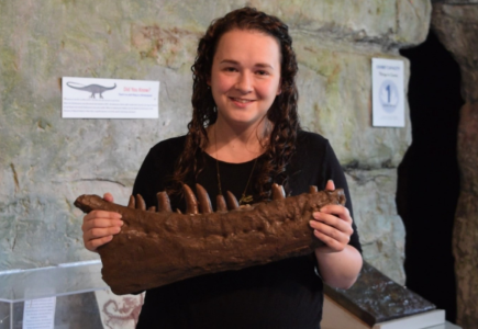 smiling woman holding a dinosaur jawbone replica 