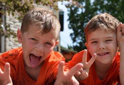 two boys looking at camera with peace signs, one smiles and one sticks out his tongue