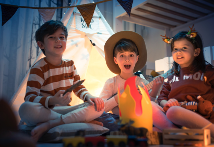 three kids in a room in front of a fake fire