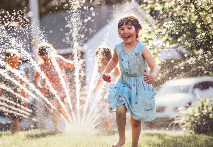 A child playing with sprinklers in the background.