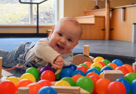 baby laying amongst multi coloured rubber balls and wooden blocks