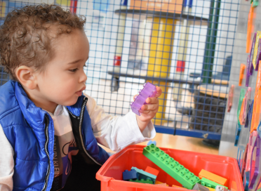 child in blue vest sorting multi-coloured blocks in front of magnetic wall covered in multi-coloured magnetic shapes